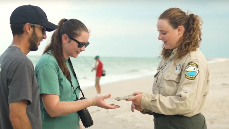 A Park Ranger interpreting to visitors on the beach about a stone that she is holding in her hand. 