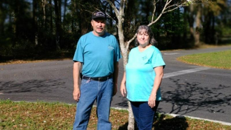 a man and woman in blue shirts stand next to a tree.