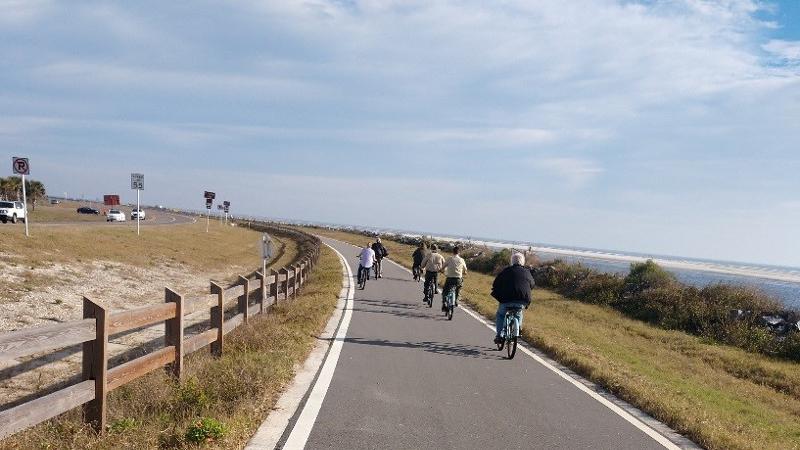 a group of bike riders pedal down a paved trail next to the coastline