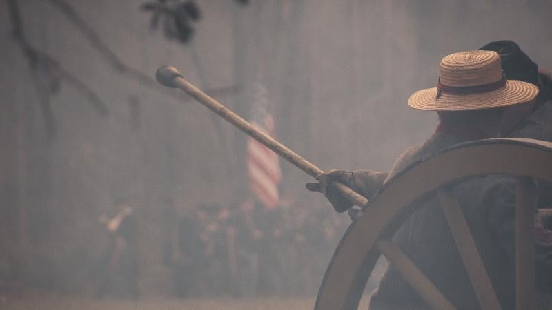 Reenactors reload cannon. US flag is visible through the smoke. 