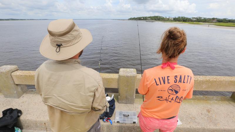 a man and woman with backs to the camera fish off of a concrete bridge