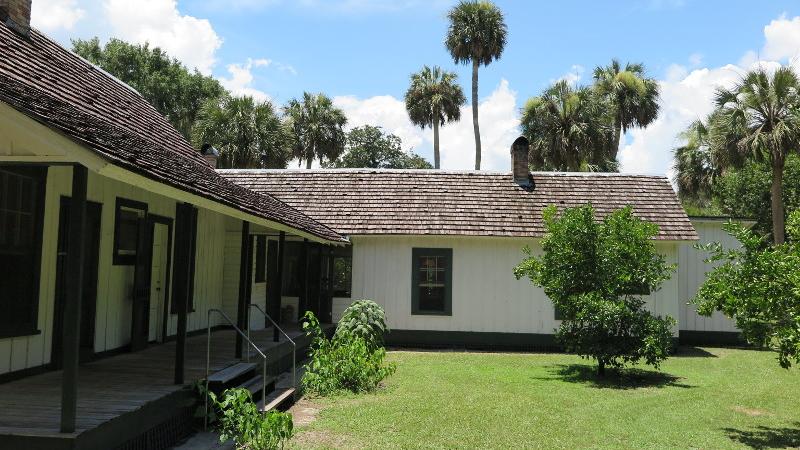 a side view of a yellow and green house surrounded by orange and palm trees