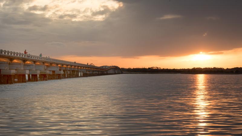 a view of a long concrete bridge at sunset