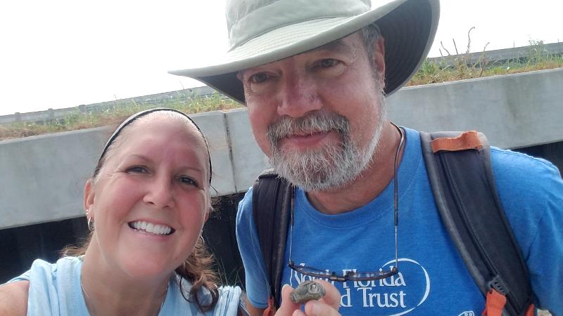 a man and woman in field clothes smile at the camera while holding some sort of small artifact