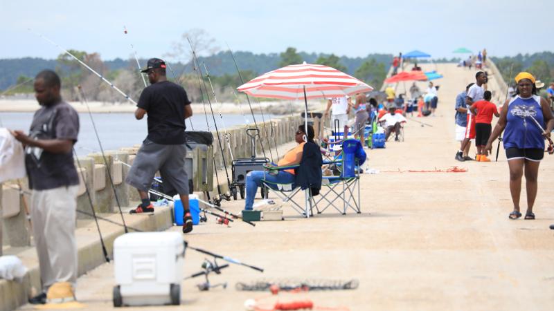 large crowds of people fish off of a long concrete bridge