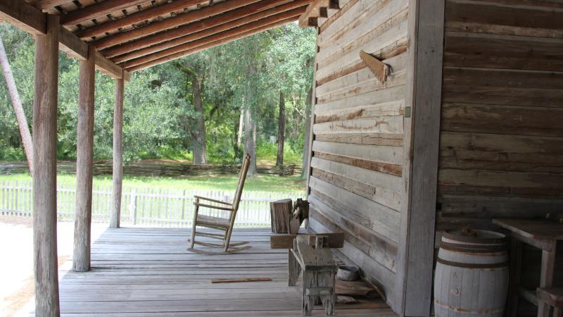 a rocking chairs sits on a wooden porch with antique farming equipment.