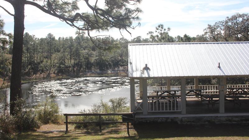 a covered picnic pavilion sits atop a bank next to a lake