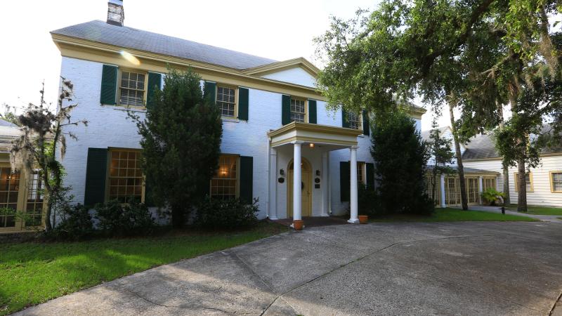 a stately mansion with green and yellow trim next to an oak tree