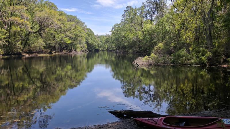 a red kayak sits on the banks of a river lined with trees