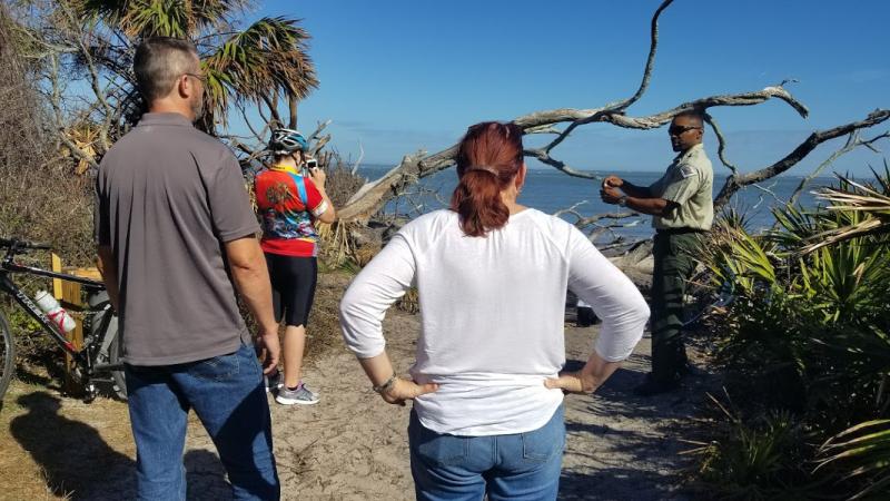 a park ranger points at a beach habitat for several visitors.