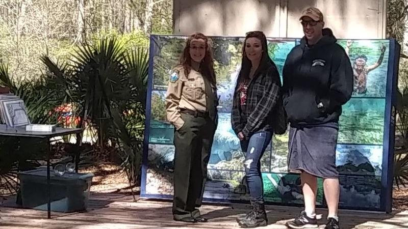 A woman in ranger uniform stands next to a man and woman on a stage