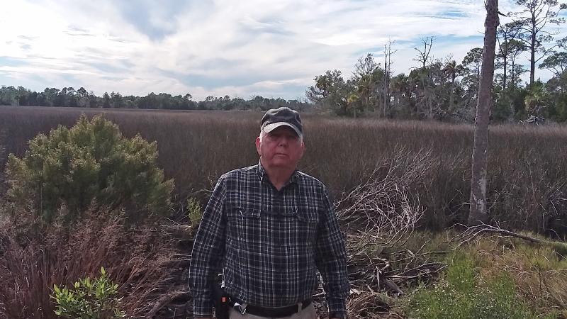 A man stands in front of a scrub habitat