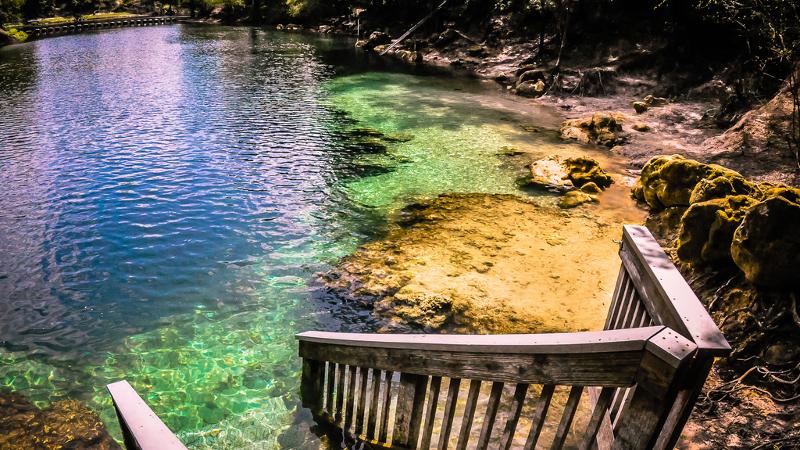 a set of stairs leads down into multi-colored water in a clear spring