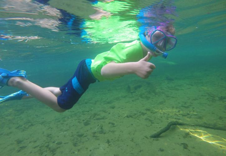 A boy swims in clear water, wearing a mask.