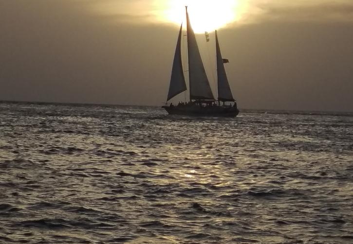 A view of a sailboat in the distance at sunset.