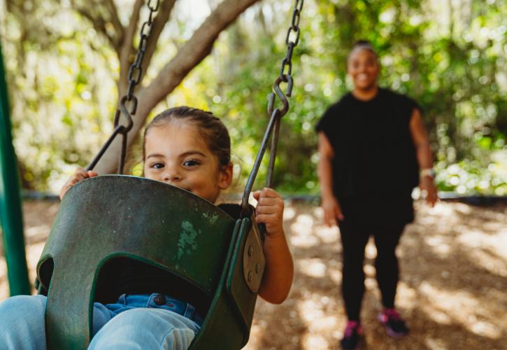 A man pushes a child, who is sitting in a child's swing.