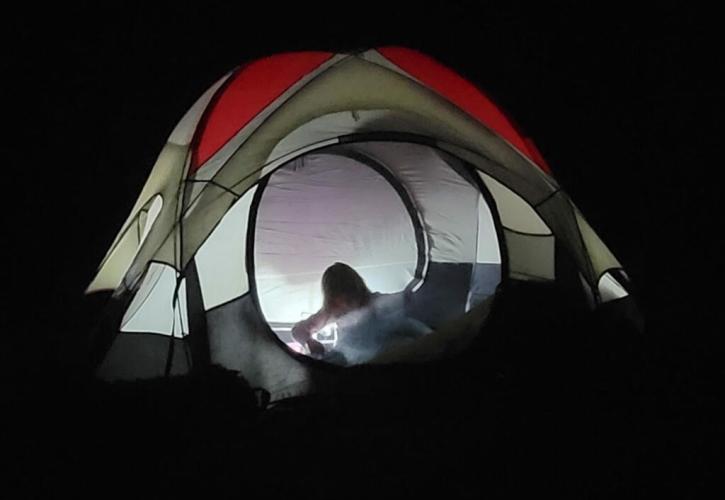 An illuminated camping tent, surrounded by darkness. Someone in the tent is reaching for something.