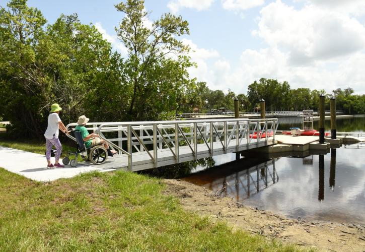 Woman pushing man in wheelchair at canoe launch to river