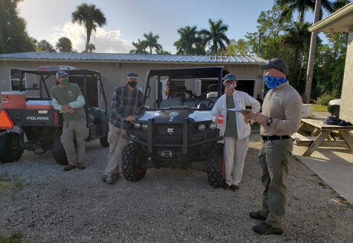 Four people standing near ATV and wearing masks preparing for trail work.