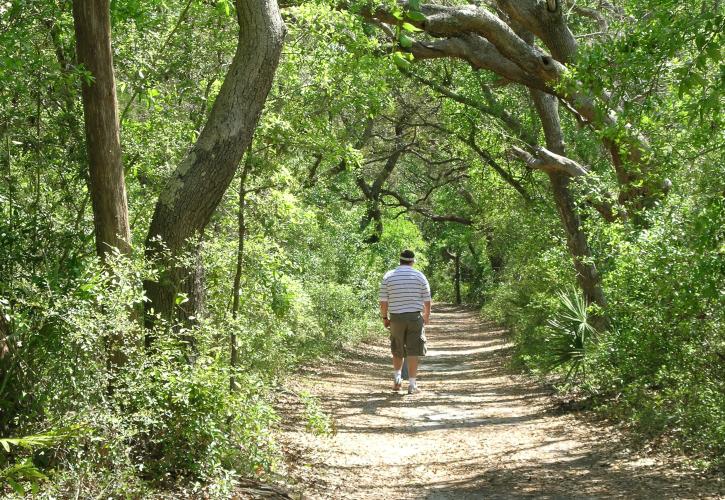 Man walking on sandy path on shaded trail.