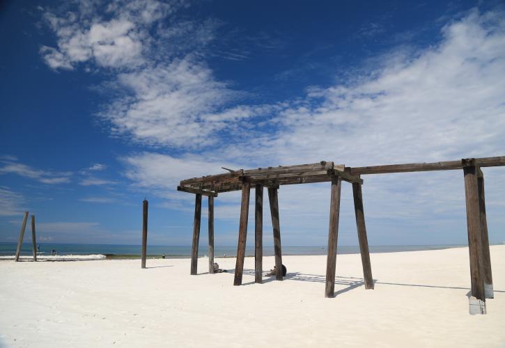 Remnants of Pier from Avondale Mills era on white sandy beach meeting blue skies.
