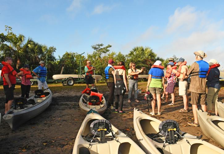 Group of people standing around canoes preparing for a paddling trip on the river.