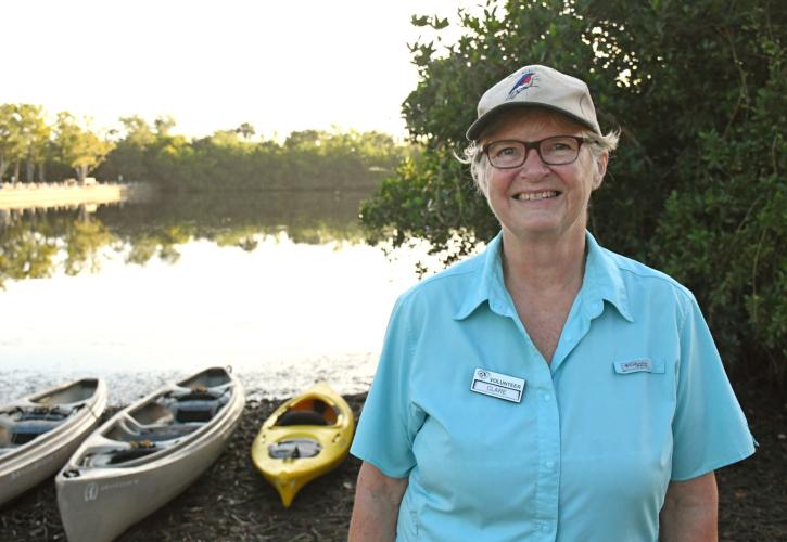 Woman wearing blue shirt standing near water and canoes