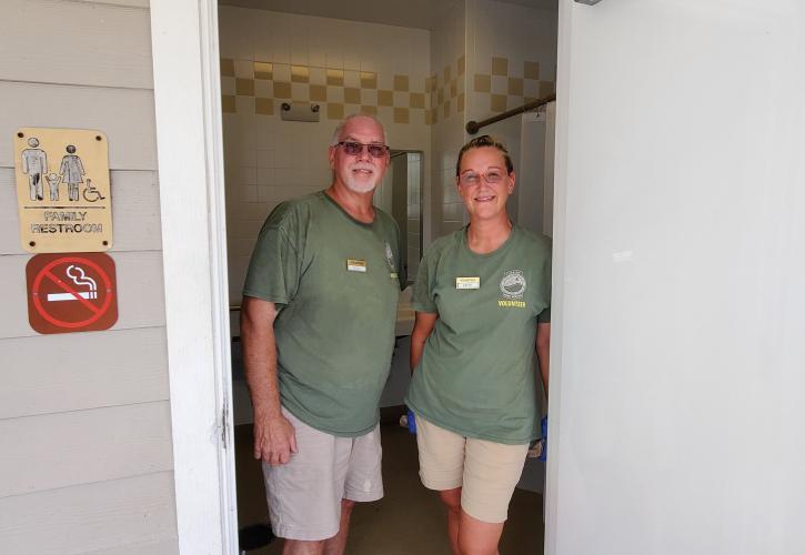 man and woman wearing green shirts tan pants cleaning restroom