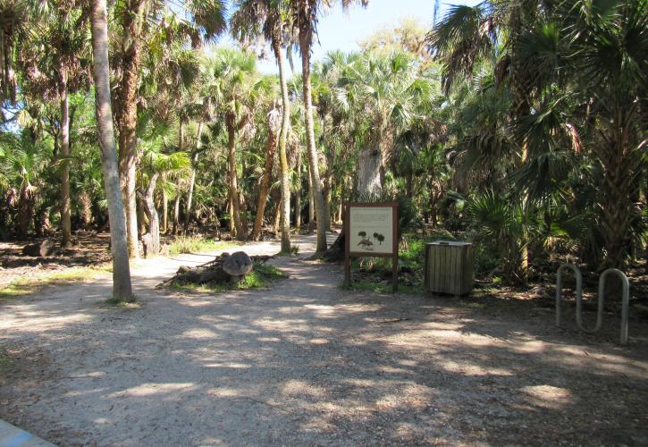 A hardpacked trail with signs, bike rack, and trash container