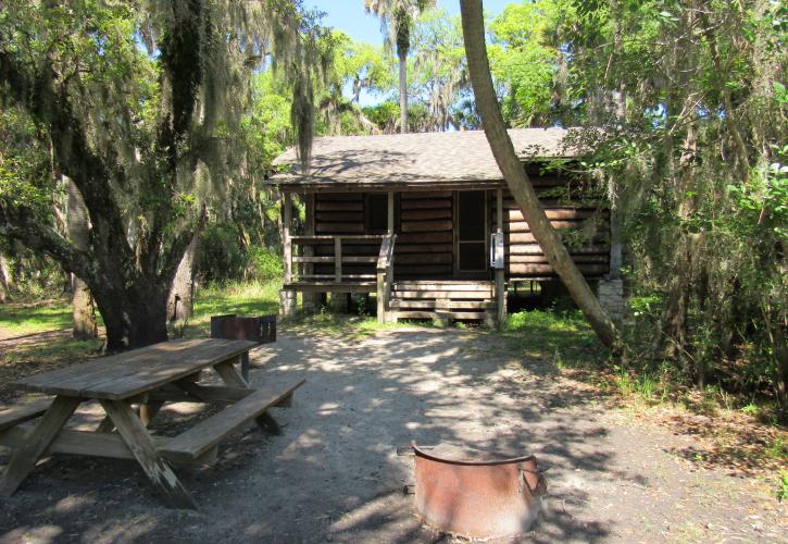 A firepit, grill, and picnic table are visible from the backside of the cabin