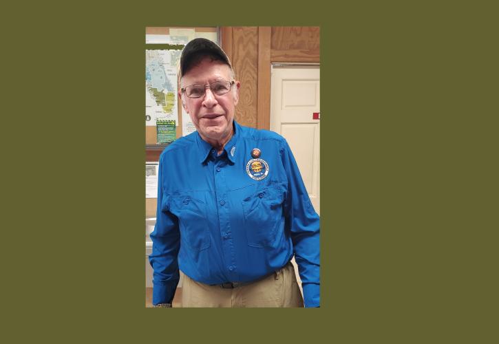 Man standing with blue shirt, ball cap and tan pants