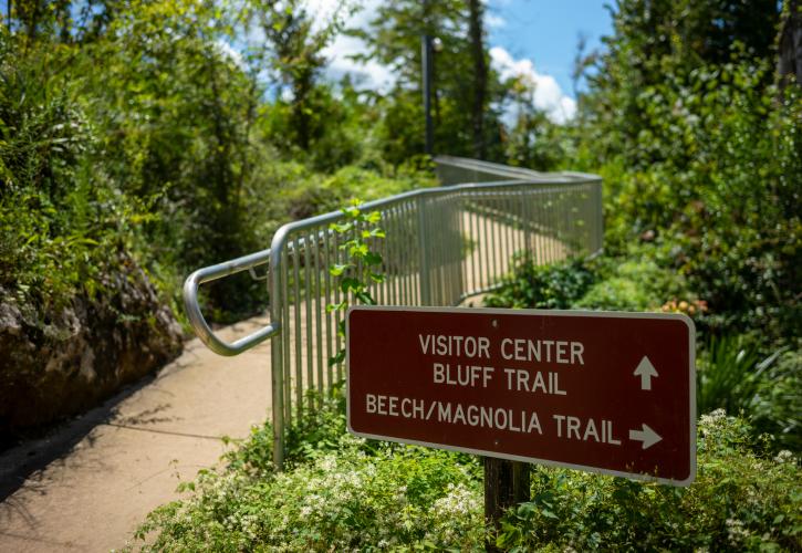 Trail sign with a metal railing and concrete path.