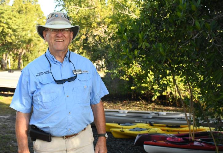 Man with Blue shirt tan pants hat near canoes