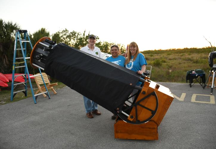 three people standing behind a homemade telescope