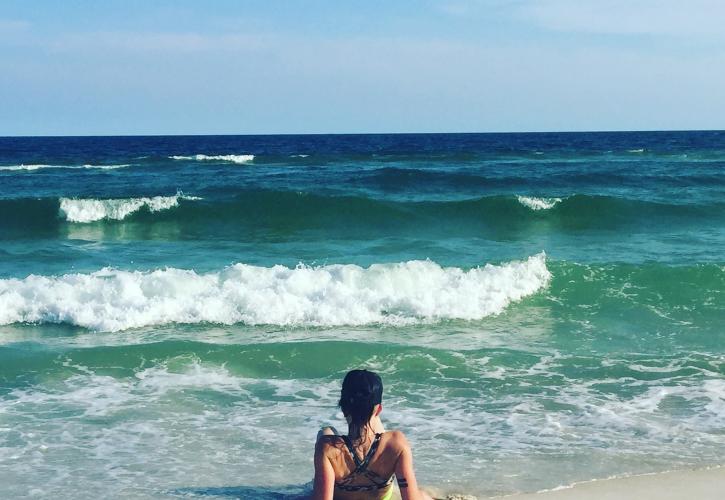 Lady sits at waters edge facing the emerald green water. 