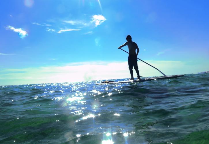 Boy paddleboards on sparkling emerald green water.