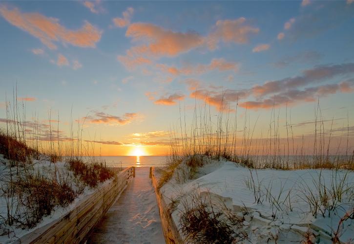 Boardwalk between white sand dunes leads to setting sun.