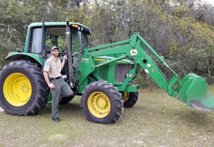 Park Ranger Kyle Blair standing next to a tractor and smiling at the camera