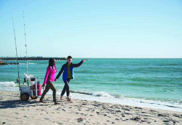Two young people pulling their wagon with fishing gear on Florida's coastline.