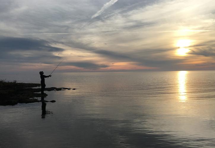 Single person fishing near open water vista with dramatic sunset in veiw