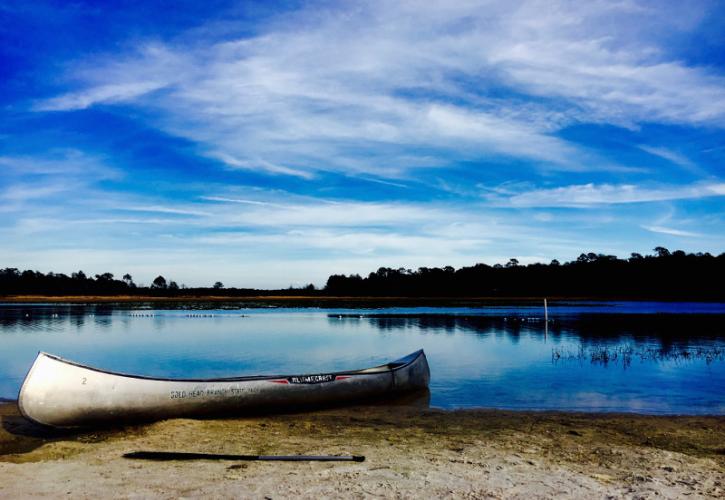 a canoe sits on the banks of a blue lake under a blue sky