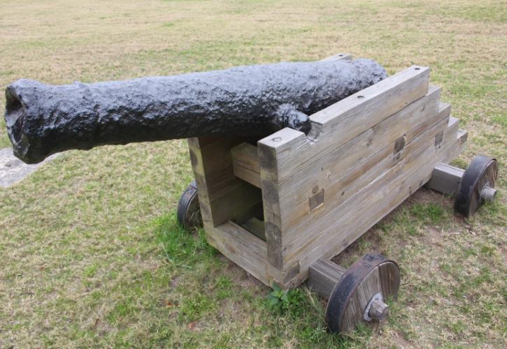 an old cannon on a wooden base with wheels sits in the grass