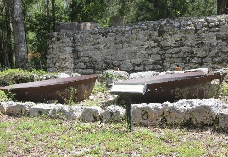 two metal kettle drums are partially submerged in the ground by an old stone wall