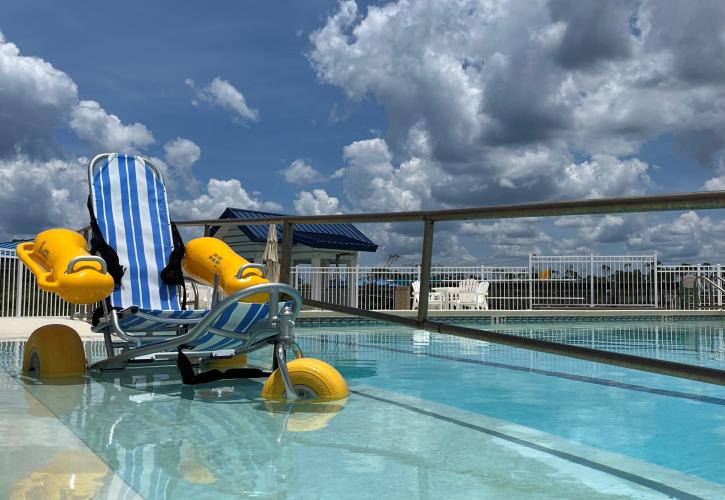 Floating wheelchair rests on ramp into swimming pool.