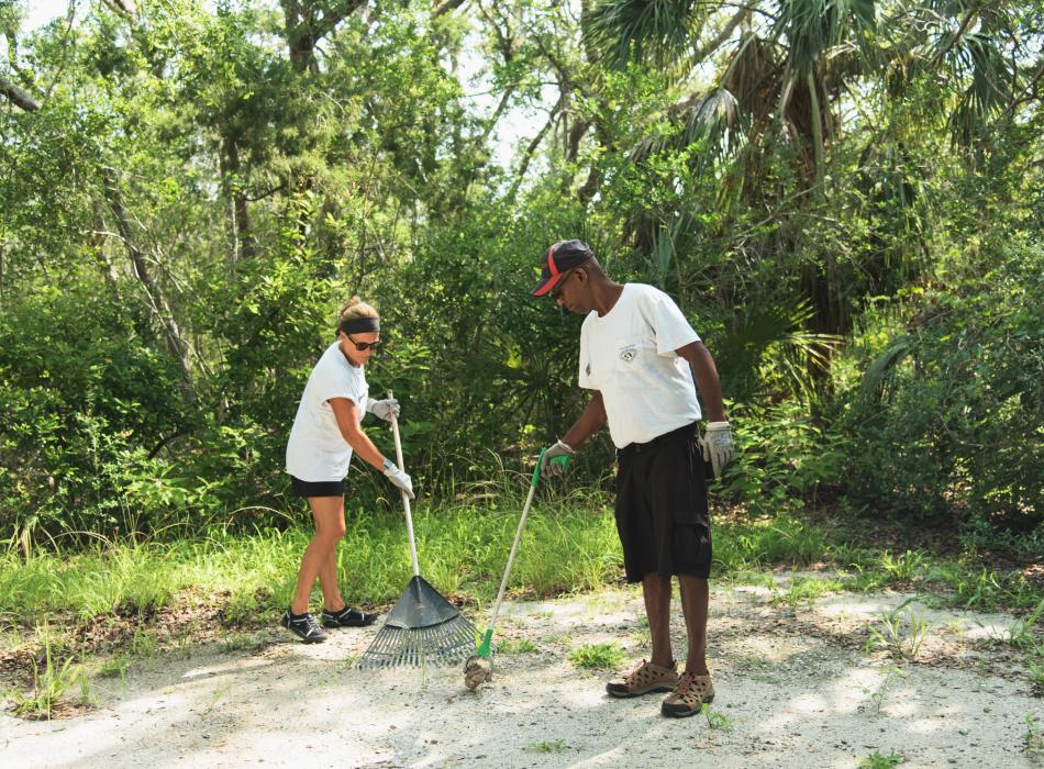 Two volunteers prepare a campsite for new campers by raking and picking up litter.