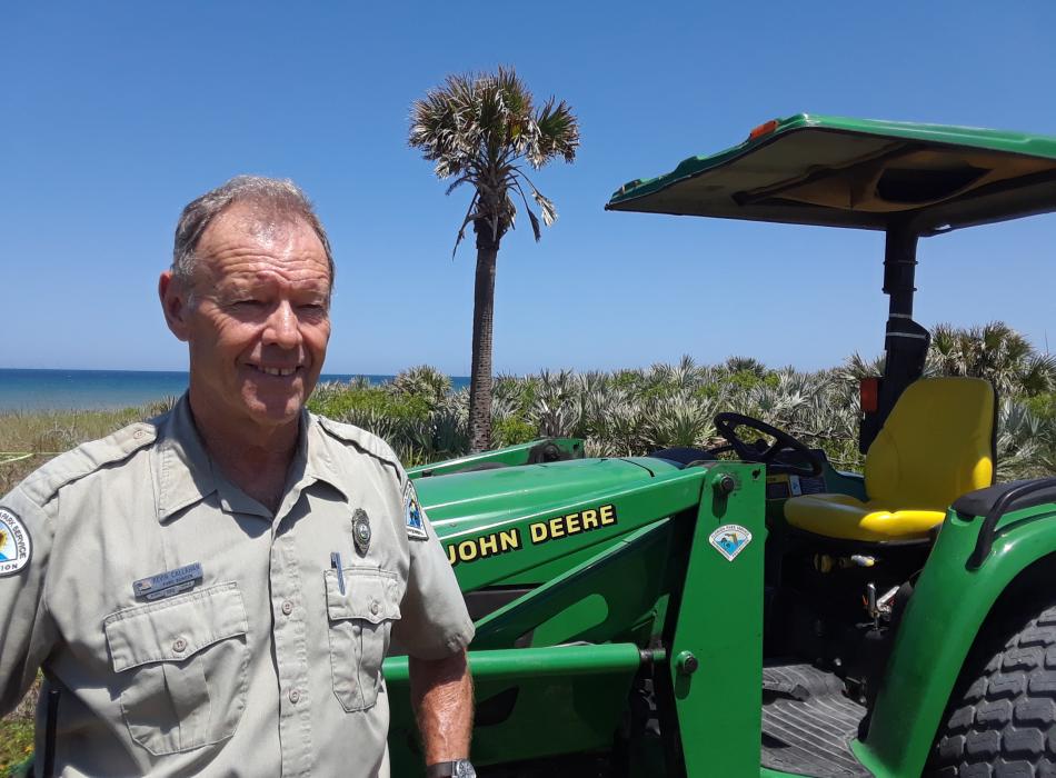 Park Ranger Kevin Callahan standing in front of the John Deere Tractor and Atlantic Ocean