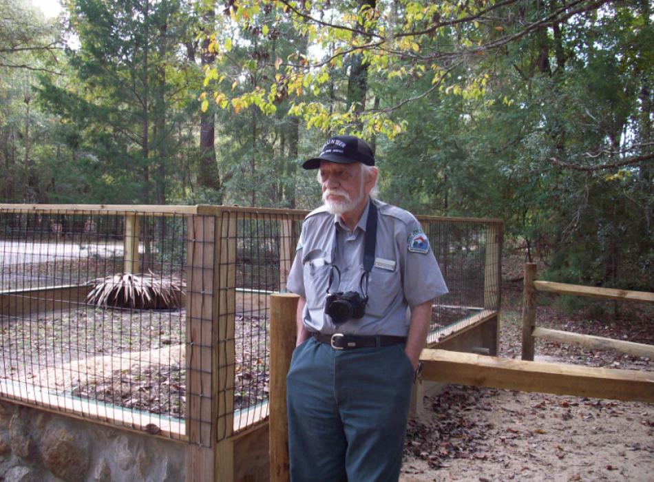 an older man in a volunteer uniform stands next to a pen with a camera