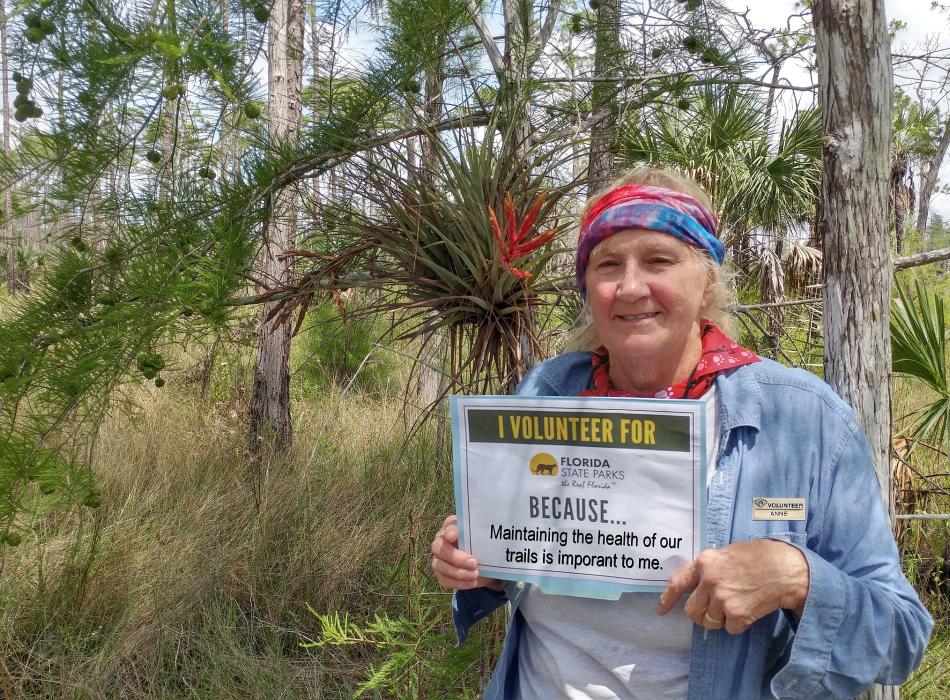 Woman standing with woods and native plants in background.