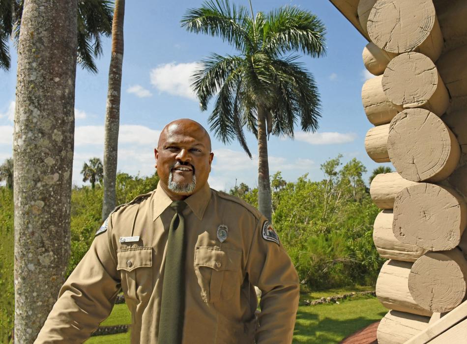 Environmental Specialist Maulik Patel standing at a log building with Royal palms in the backgound.