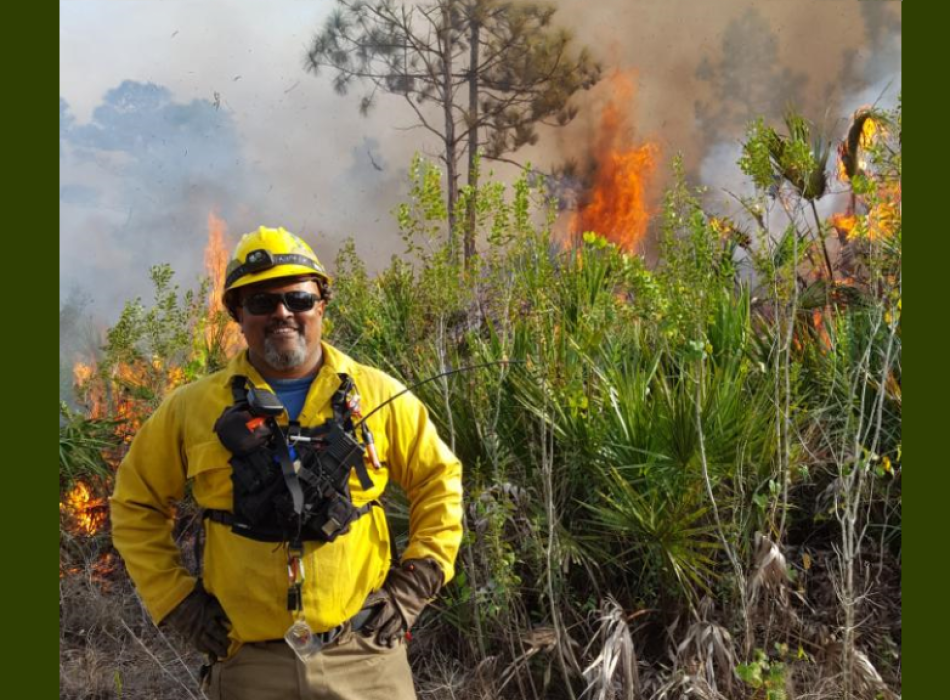 Park Environmental Specialist Maulik Patel wearing fire protection gear with active fire in the background.